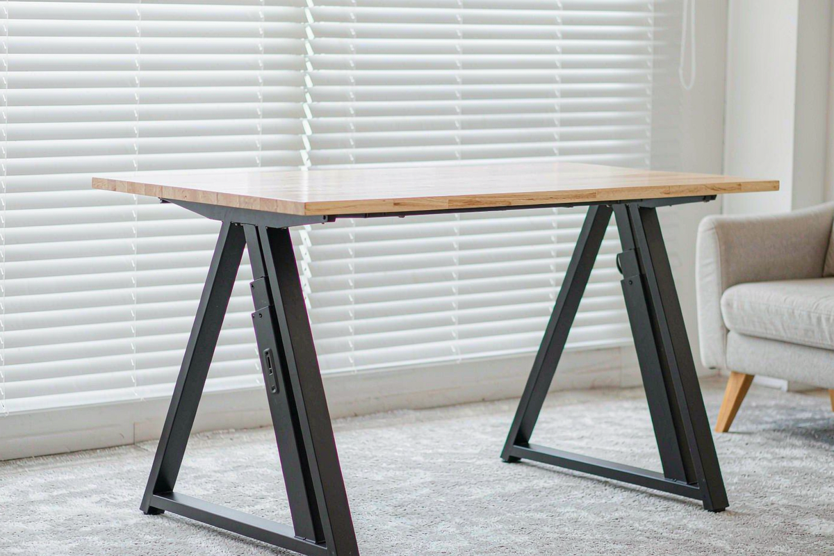 FlexiSpot E6 Max standing desk frame with a light wood top, raised