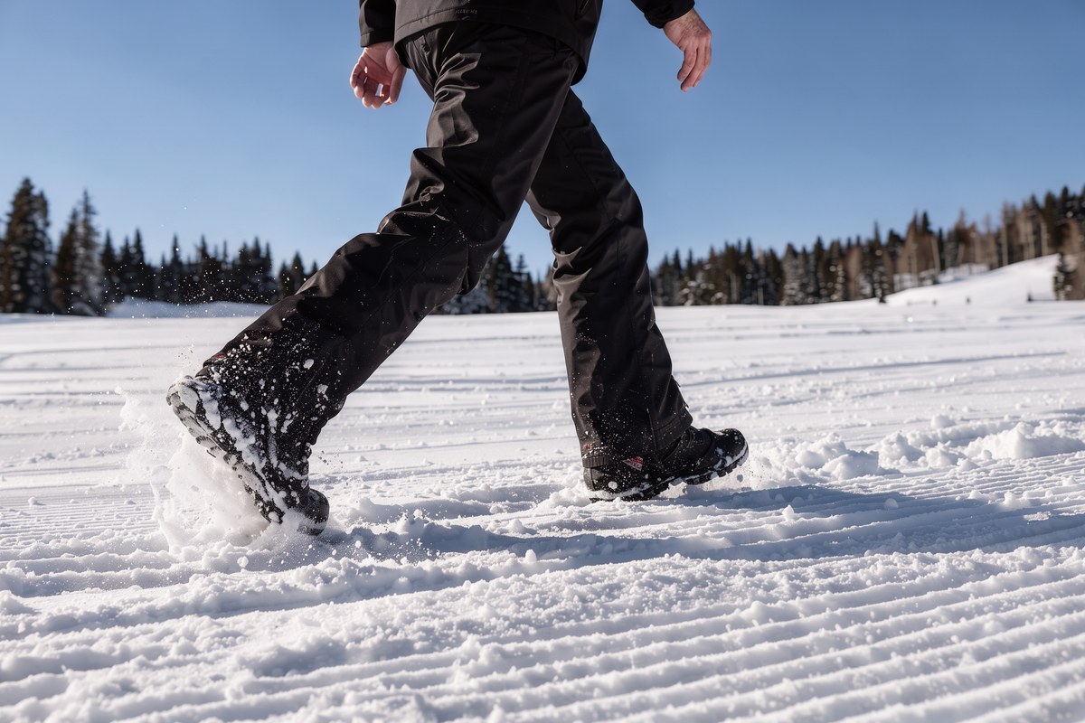 A skier wearing black fleece-lined TACVASEN waterproof ski pants walking through fresh snow