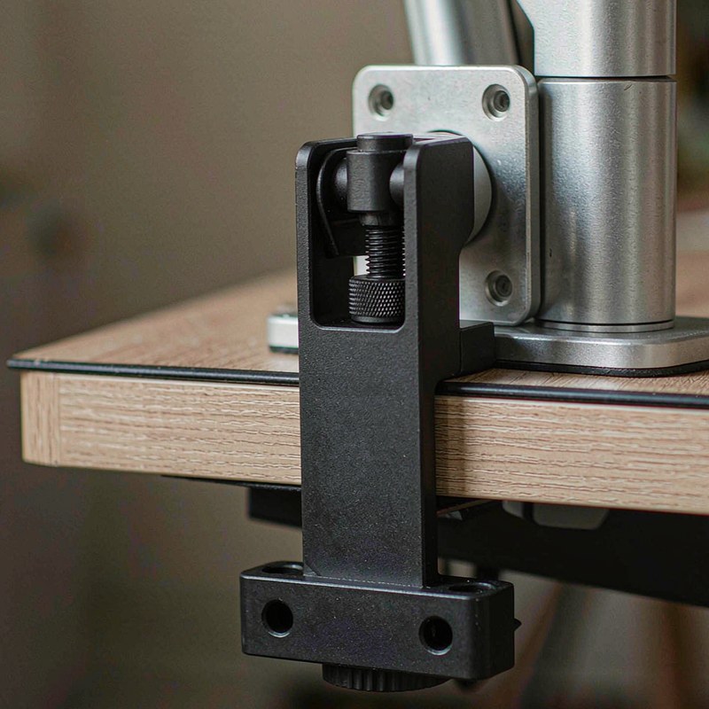 The clamp plate and threaded pad gripping a desk edge next to the VESA base.