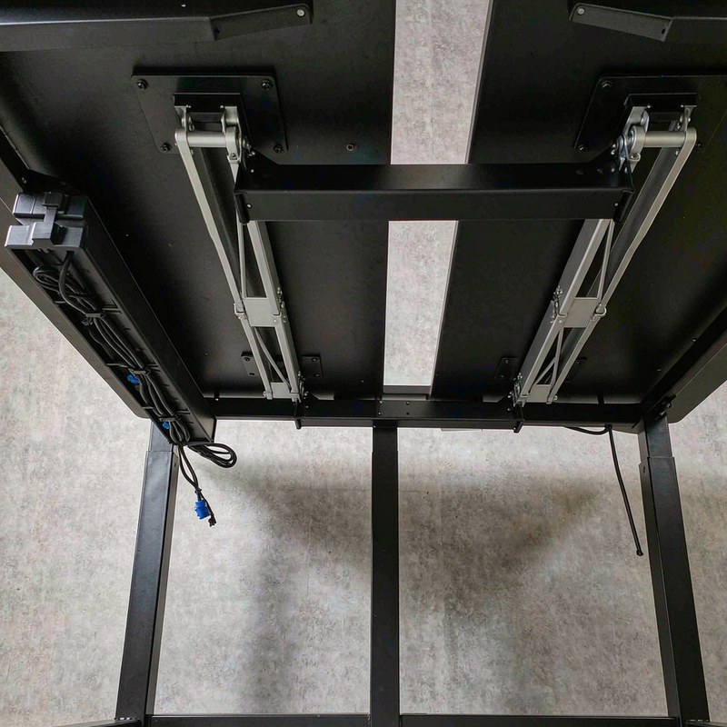 The underside of the L-shaped desk showing two lifting columns, a crossbar and a cable tray.