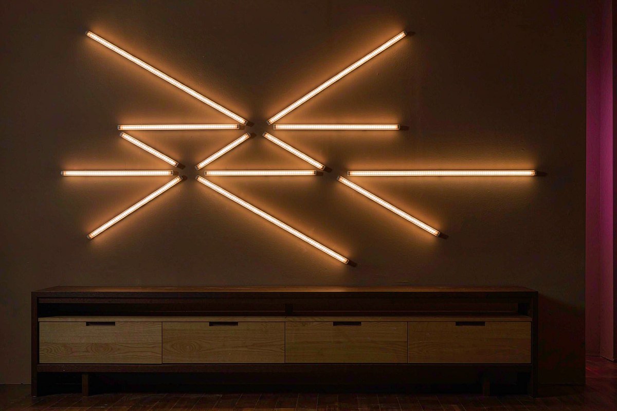 Nine Nanoleaf Lines light bars glowing in an angular pattern on a charcoal living room wall